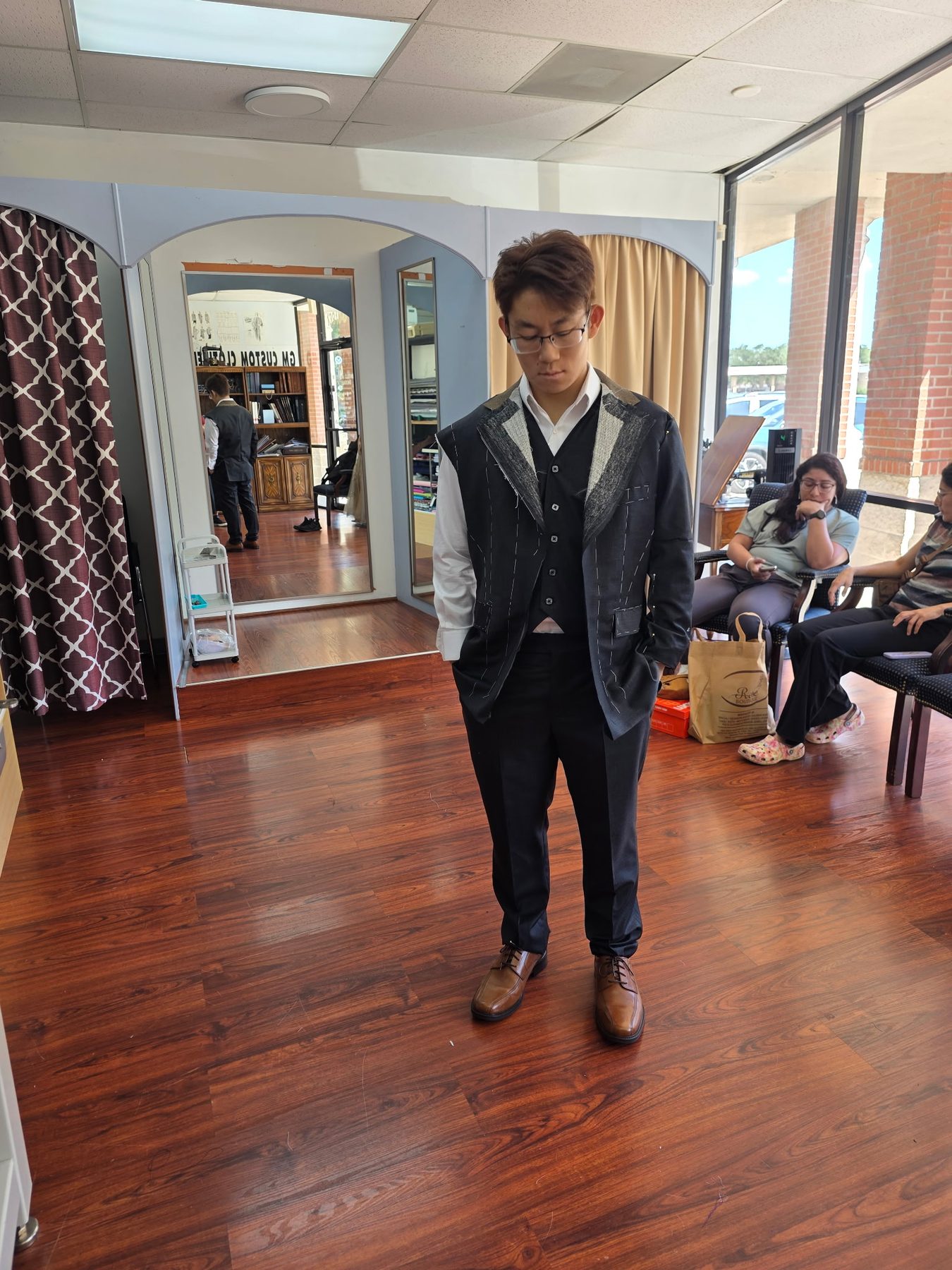 Client mid-fitting in a hand-basted three-piece suit, raw canvas and pins visible, at GM Custom Clothier in Sugar Land, TX